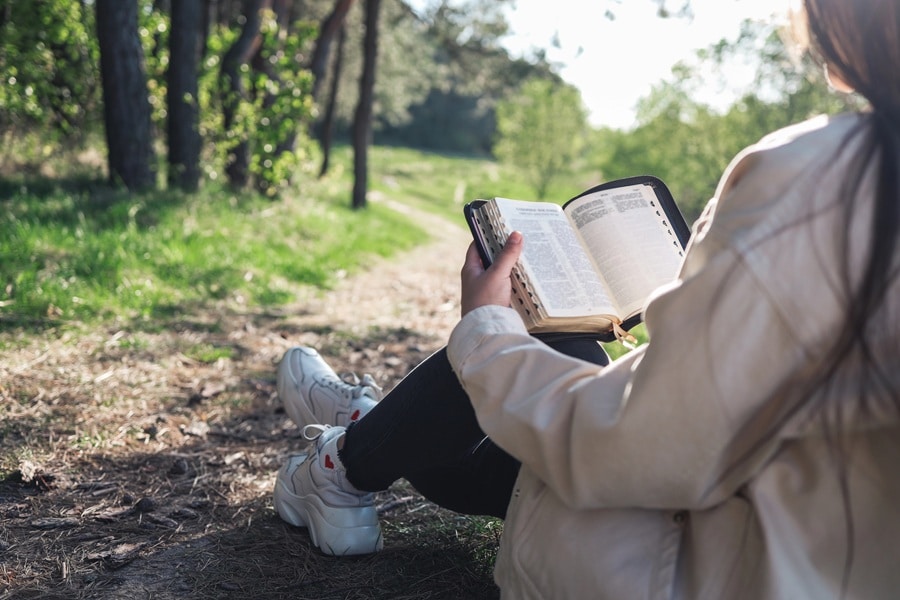 Woman reading Bible outdoors and staying focused during prayer in nature