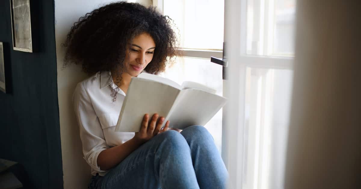 a woman sitting on a window sill reading a Christian book a woman sitting on a window sill reading a Christian book