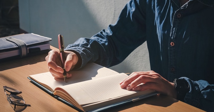 Man sitting at a desk writing his prayer in a journal. Man sitting at a desk writing his prayer in a journal.
